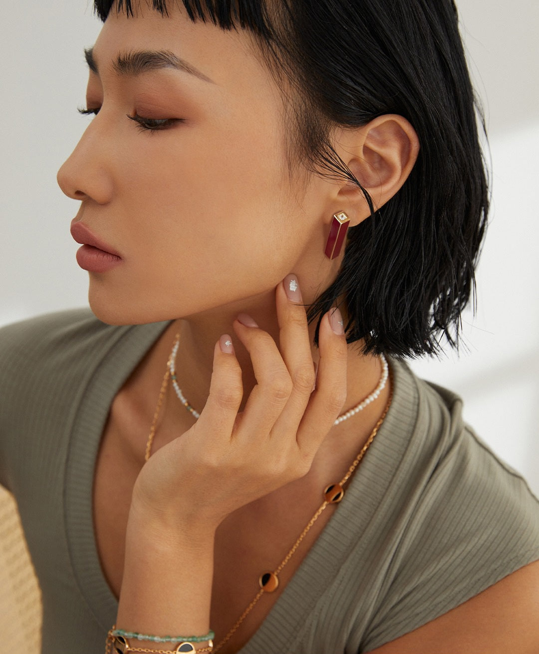 an asian model wearing a Minimalist gold earrings with red drip glaze detail on her ear